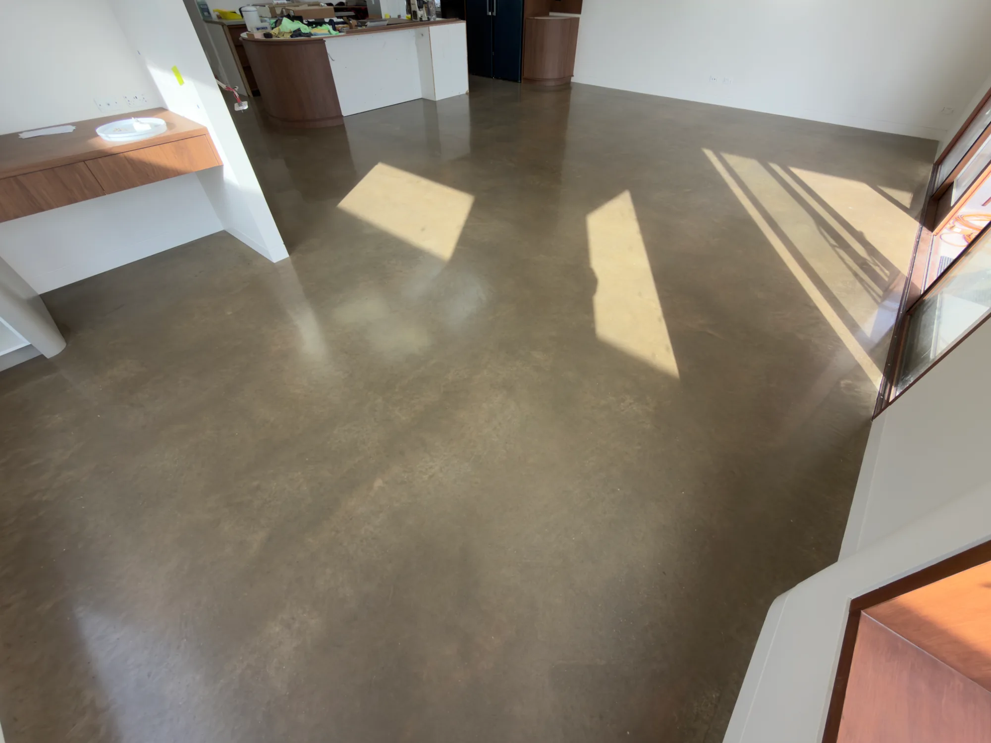 Warm grey surface-polished concrete beside timber joinery, with angular patches of sunlight across the floor