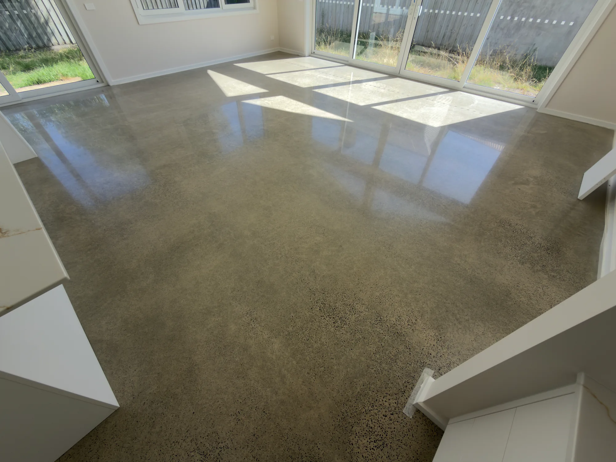 Gloss-polished concrete with scattered aggregate reflecting large windows in a Queenscliff interior